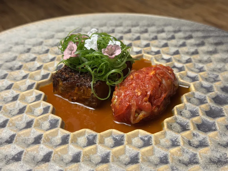 Het opgemaakte bord: Tomaten kimchi shortrib/ kimchi saus/ burned focacia/ lente ui/ lente bloemen